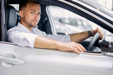 young caucasian businessman sits inside of car, elegant guy in white formal shirt look at camera and smile