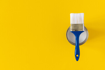 Can of white paint with a blue brush on a yellow background, painting, top view