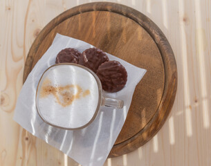 a cup of warm cappuccino and three biscuits on a wooden table
