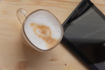 cappuccino in a glass and mobile device on a wooden table