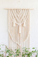 Handmade macrame. 100% cotton wall decoration with wooden hanging on white wall.  Female hobby.  ECO friendly modern knitting DIY natural decoration concept in the interior