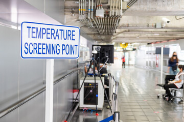 Selective focus at sign in front of the entrance of Airport terminal. Temperature screening point with thermal detection camera to scan and check body temperature to prevent Coronavirus. - Powered by Adobe