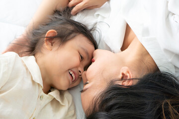 asian mother with smiling face looking at her young daughter and lying on the bed. family together and relationship