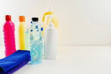 Plastic bottles of cleaning products set with pile clothes on white table background.