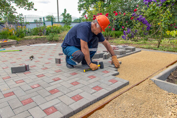 A gloved craftsman lays paving stones in layers. Brick paving slabs for professional use. Laying gray concrete paving slabs in the courtyard of the house on a sandy foundation.