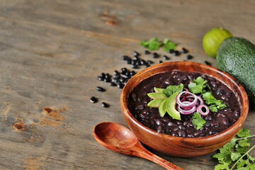 black bean soup or stew. stewed black beans served with avocado and red onion and cilantro. place for text.