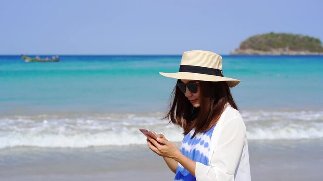 Young asian woman traveler using her smartphone at tropical sand beach, Summer vacation concept	
