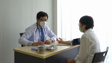 asian doctor using automated digital sphygmomanometer to measure blood pressure of senior woman patient that visit at the hospital because of hypertension. healthcare and medical concept