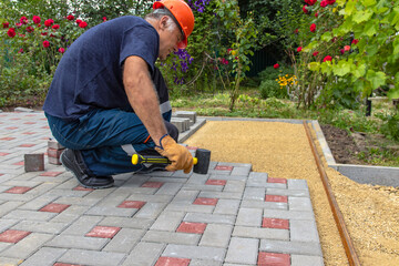 A gloved craftsman lays paving stones in layers. Brick paving slabs for professional use. Laying gray concrete paving slabs in the courtyard of the house on a sandy foundation.