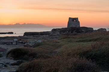 Alba sul mare con torre costiera e cielo arancione.