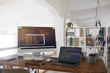 Background image of black and orange programming code on computer screen and laptop in contemporary...