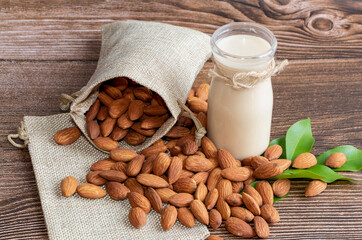 Almond milk in glass with almonds on wooden table