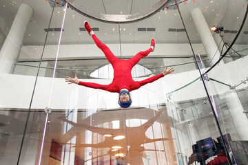levitation of sports people in a wind tunnel. jumping without a parachute in a wind tunnel indoors. Man in a red suit, portrait of a skydiver,  flies head down. extreme sport - obrazy, fototapety, plakaty
