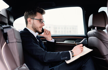 Businessman in specs writing in notebook sitting in his car