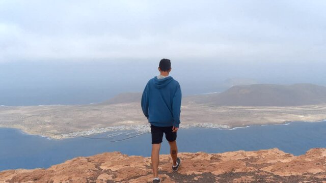 hombre joven en la cima de un acantilado, observa la isla de la Graciosa. Lanzarote. Islas Canarias