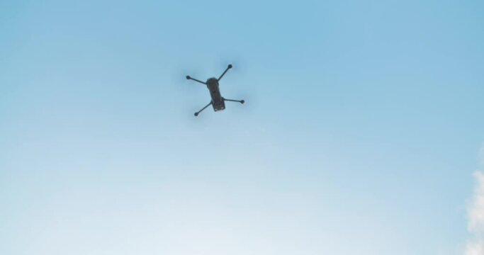 Takeoff drone flies on bright blue sky background. Modern technologies for shooting photos and videos from above. Slow motion shot. Flight overhead