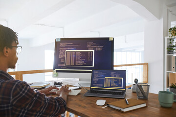 Portrait of African-American IT developer typing on keyboard with black and orange programming code...