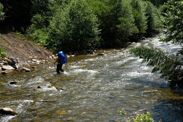 Hiker man crossing a river using trekking poles