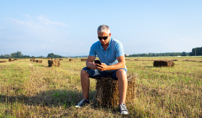 Fototapeta na wymiar Adult man with a phone sits on a haystack.