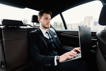 Busy businessman using his laptop in luxury car