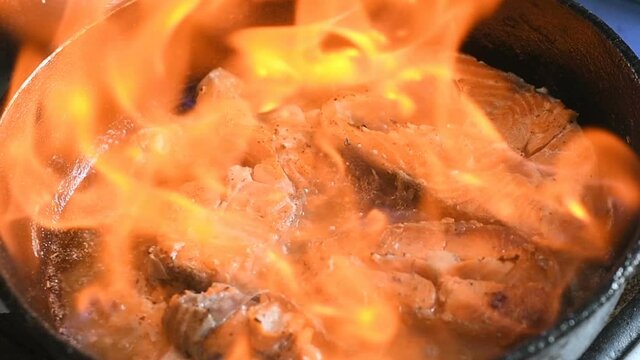 Frying pan with red sea fish stakes, trout or salmon, flaming burning fire. Cooking seafood stove kitchen cuisine, cafe or restaurant dish, delicious tasty fancy food concept. Slow motion