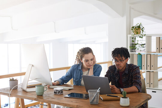 Portrait Of Two Young IT Developers Working On Project Together While Sitting At Desk And Using Computer In Modern Office Interior, Copy Space