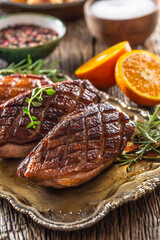 Juicy roasted duck breasts on a vintage table with rosemary, cut orange, salt and pepper