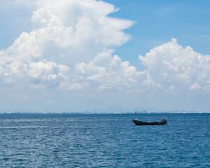 A man sits on a boat and fishing in the sea under blue sky with cloud.