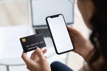 Close up over shoulder view of woman hold smartphone and credit card shopping online on gadget,...