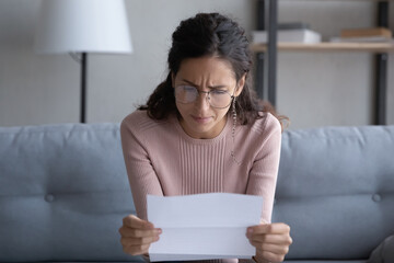 Worried young Caucasian woman in glasses read post paper letter think of bad news or problem in...