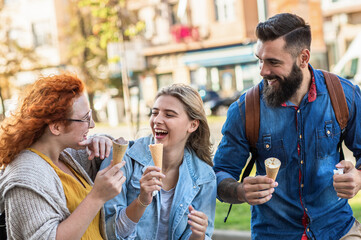 Group of tourists enjoying on vacation, young friends having fun walking on city street eating ice cream during  the day.
