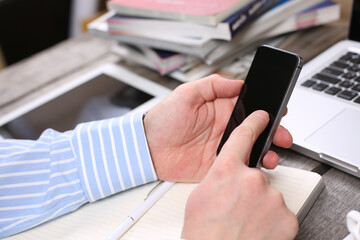 Hand hold phone on stylish workspace with computer and posters on home or studio