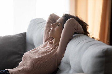 Young woman sit relax on sofa in living room, sleep or take nap relieving negative emotions, calm...