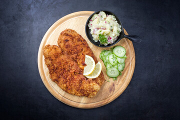 Traditionelle fittierte Wiener Schnitzel mit Kartoffel und Gurkensalat angeboten als Draufsicht auf einem rustikalen Holz Board mit Textfreiraum