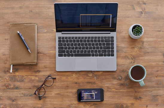 Top down view background composition of laptop and smartphone with computer code on textured wooden desk in office, copy space
