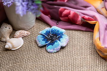 Handmade sequin brooch in the shape of a blue flower. Brooch as a gift and talisman. Handmade jewelry on a fabric background. Selective focus, close-up, composition.