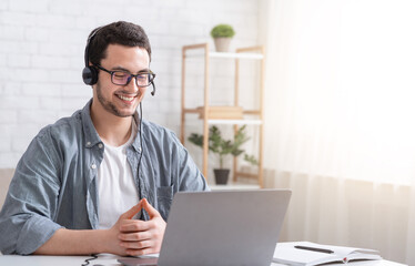 Learn english online. Smiling guy with headphones looking at laptop, talking with teacher