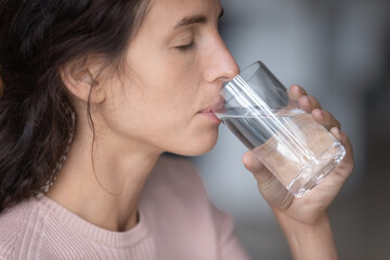 Close up of thirsty young caucasian woman hold glass drink clean still mineral water for body...