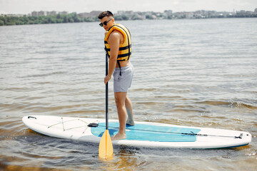 Handsome man with a sup. Surfer in a yellow vest.