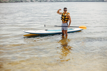 Handsome man with a sup. Surfer in a yellow vest.