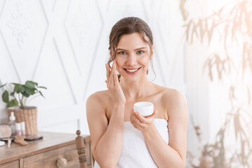 Attractive young woman applying face cream at home