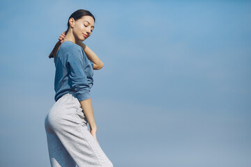 Beautiful girl training on a sky background. Woman in a blue sweater. Lady make a yoga