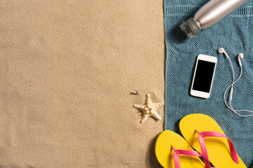 Top view straw hat,headphones and smartphone with copy space. Traveler accessories on sand. Travel vacation concept. Summer background. Border composition made of towel