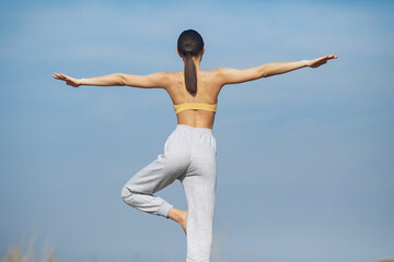 Obraz premium Beautiful girl training on a sky background. Woman in a yellow top. Lady make a yoga