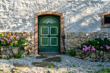Old farmhouse made of fieldstones with a wooden door, a window and bright flowers