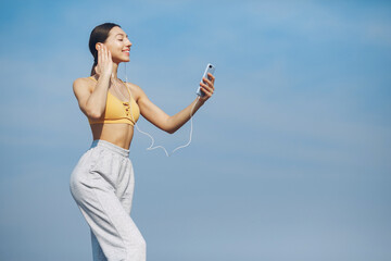 Beautiful girl standing on a sky background. Woman in a yellow top. Lady with phone in her hands