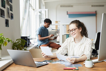 Portrait of young woman reviewing photographs while working on editing and publishing in modern office, copy space
