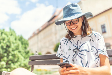 Young tourist smiling into her cell phone sitting on a bench in the old town center