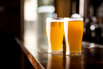 Friends meeting at pub. Two glasses of light beer with foam on wooden bar in pub