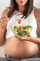 Pregnant girl eats salad from a bowl in her hand